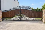 Artystyczna kuta brama uchylna z wypełnieniem drewnianym i motywami winogron, model BU81 — odtworzone ujęcie oryginalne. Wizualizacja AI.
