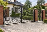 Kuta brama wjazdowa dwuskrzydłowa z elementami ornamentalnymi, model BU47 — aranżacja europejskiej posesji z dopasowanymi elementami ogrodzenia. Wizualizacja AI.