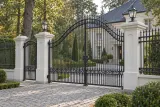 Kuta brama wjazdowa dwuskrzydłowa z łukowym nadprożem i klasycznymi zdobieniami, model BU56x — aranżacja europejskiej posesji z dopasowanymi elementami ogrodzenia. Wizualizacja AI.