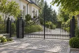 Kuta brama wjazdowa uchylna z ozdobnymi ornamentami, model BU86 — aranżacja europejskiej posesji z dopasowanymi elementami ogrodzenia. Wizualizacja AI.