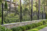 Kute ogrodzenie ozdobne z motywami secesyjnymi, model mg04 — aranżacja: zaciszna willa wśród sosen z niską kamienną podmurówką. Wizualizacja AI.