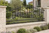 Kute ogrodzenie panelowe z ornamentem floralnym, model OK84 — aranżacja: spokojny ogród kamiennego domu z wapienną podmurówką. Wizualizacja AI.