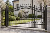Kute ogrodzenie posesyjne z ornamentyką klasyczną i grotami wiktoriańskimi, model OK76 — aranżacja: tradycyjna willa z szarymi słupkami i wiosennym ogrodem. Wizualizacja AI.