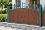 Kute ogrodzenie posesyjne z panelami stalowymi imitującymi drewno, model OK87 — aranżacja: współczesny dom z drewnem i tynkiem przy jasnym chodniku. Wizualizacja AI.
