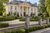 Kute ogrodzenie rezydencjalne z ornamentyką klasyczną, model ok162 — aranżacja: historyczna kremowa willa z szarymi słupkami kamiennymi. Wizualizacja AI.