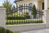 Kute przęsło ogrodzeniowe z łukowym zwieńczeniem i elementami ornamentowymi, model OK39 — aranżacja: klasyczny kremowy dom z jasnymi słupkami kamiennymi. Wizualizacja AI.