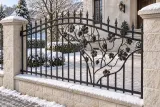 Kute przęsło ogrodzeniowe z ornamentyką winorośli, model OK38 — aranżacja: miejska willa z jasnymi słupkami kamiennymi i brukowanym dziedzińcem. Wizualizacja AI.